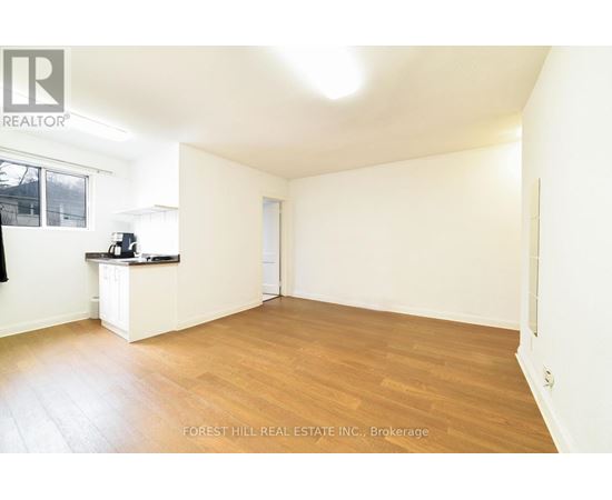 A spacious room with wooden flooring and white walls, with a window on the left side.