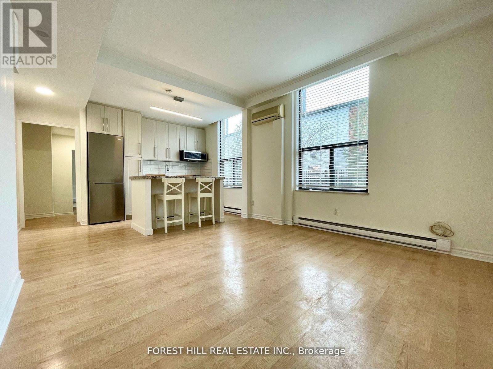 A spacious living room with wooden flooring and a kitchen area in the background.