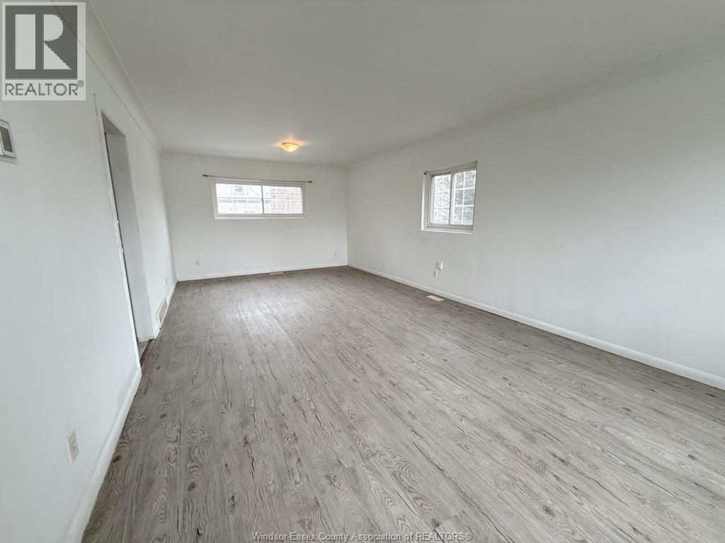 A spacious room with wooden flooring and two windows.