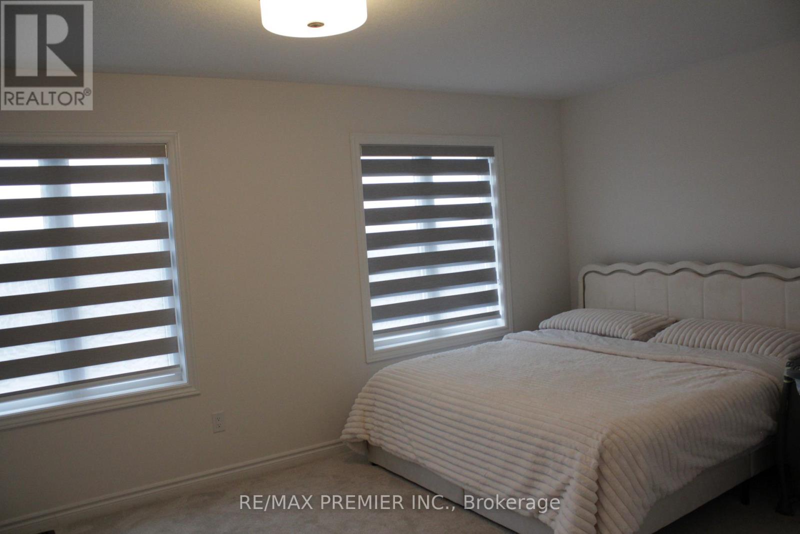 A bedroom with a bed, two windows with blinds, and a light fixture on the ceiling.