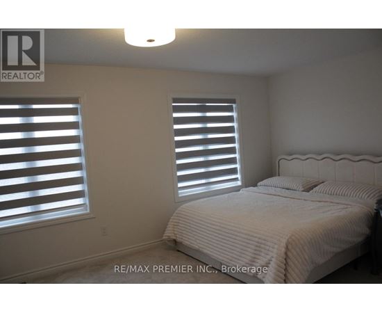 A bedroom with a bed, two windows with blinds, and a light fixture on the ceiling.