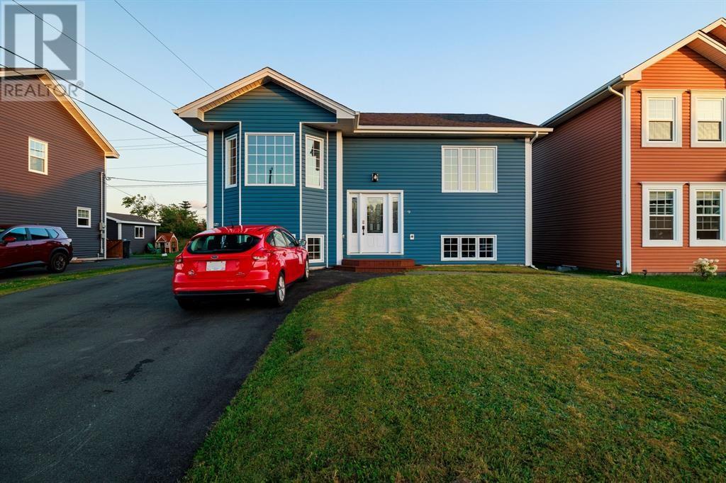 A red car is parked in front of a blue house.