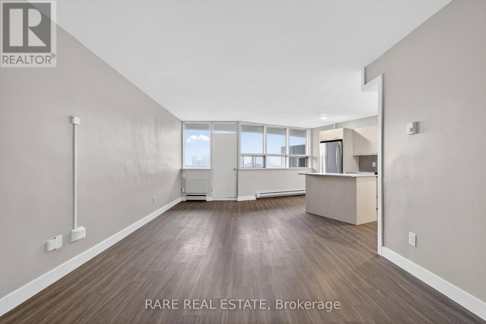 A spacious room with wood flooring and a large window.