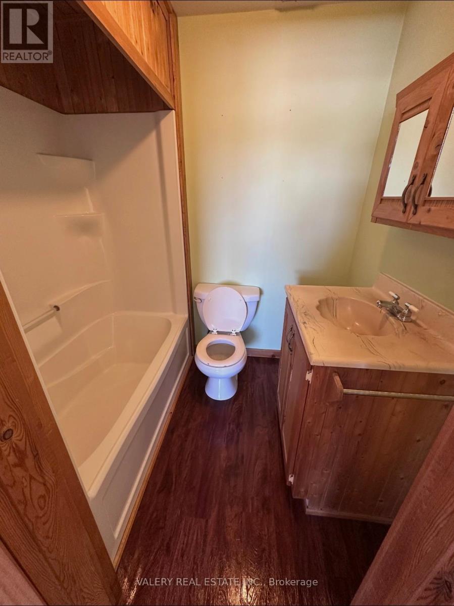 A white toilet sits in a bathroom with wooden cabinets and a bathtub.