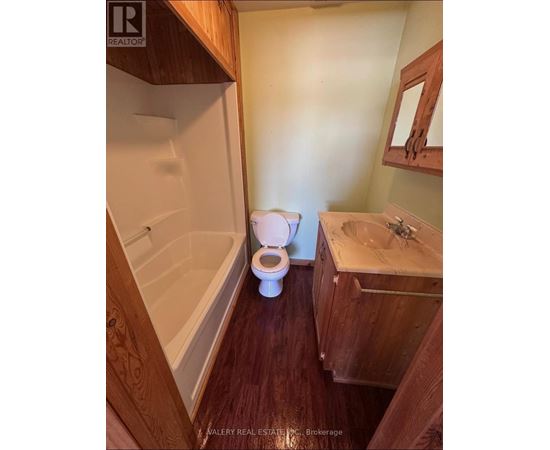 A white toilet sits in a bathroom with wooden cabinets and a bathtub.