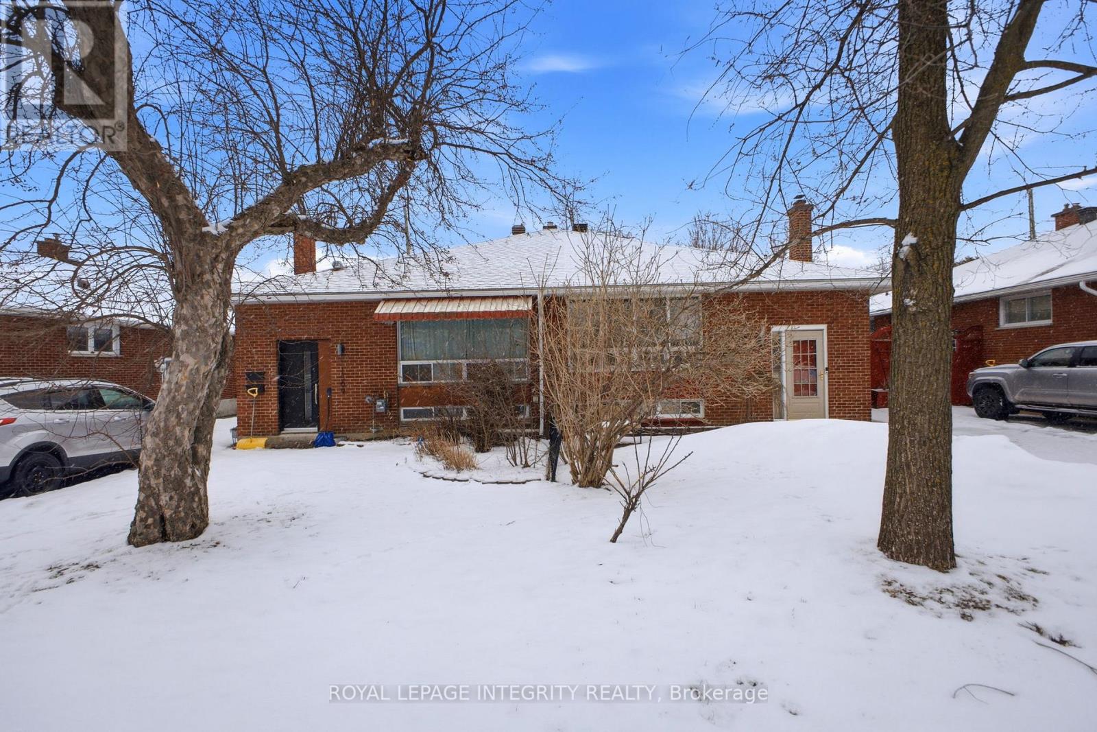 A snow-covered yard with a house and bare trees.