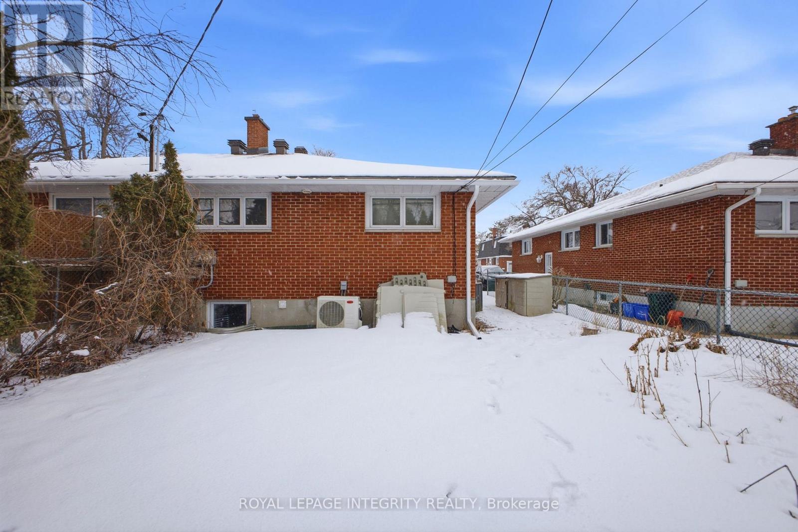 A snow-covered yard with a brick house and a fence.