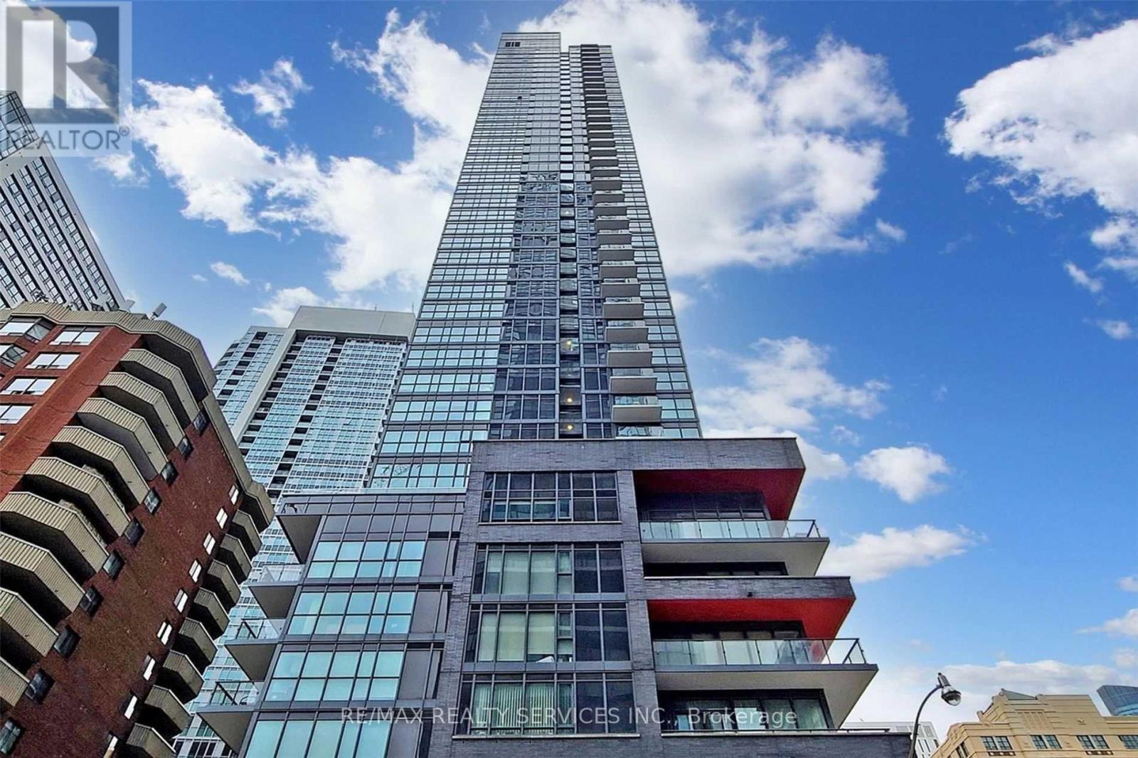 A tall building with a glass facade stands in front of other buildings.