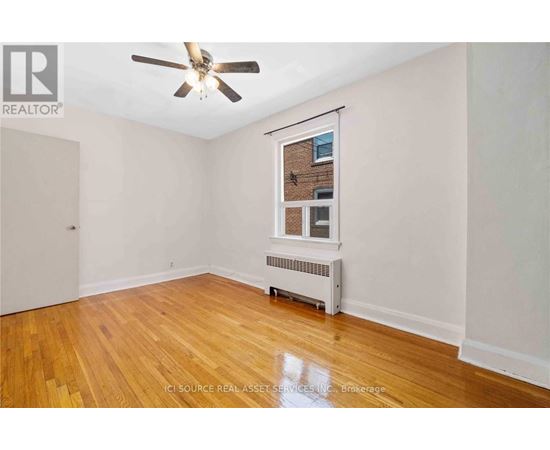 A room with a ceiling fan and a window with a view of a brick building outside.