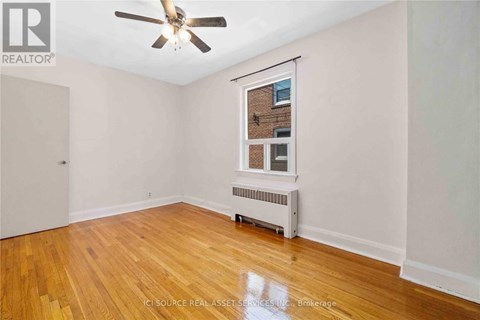 A room with a ceiling fan and a window with a view of a brick building outside.
