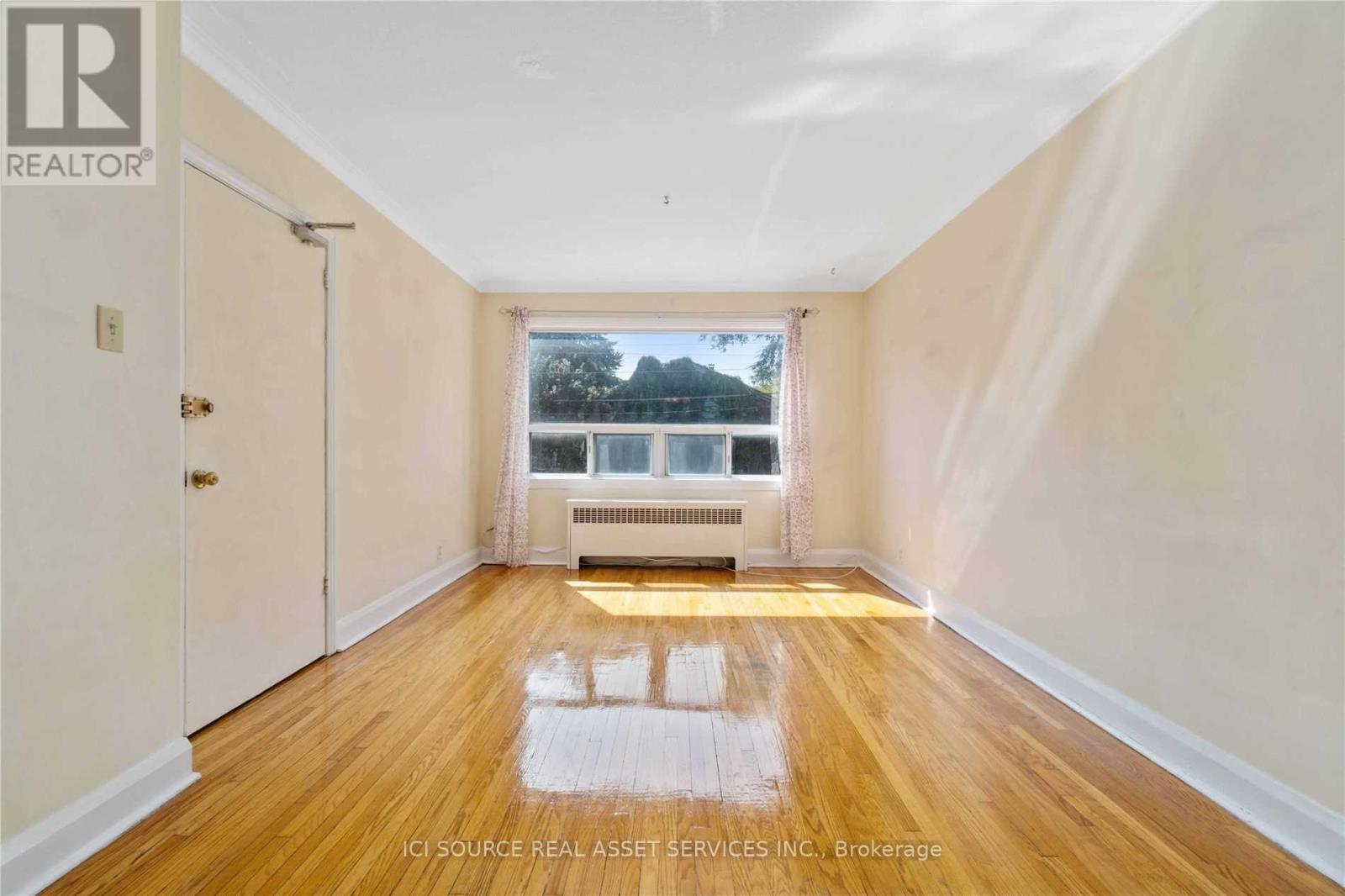 A room with wooden floors and a window overlooking a tree.
