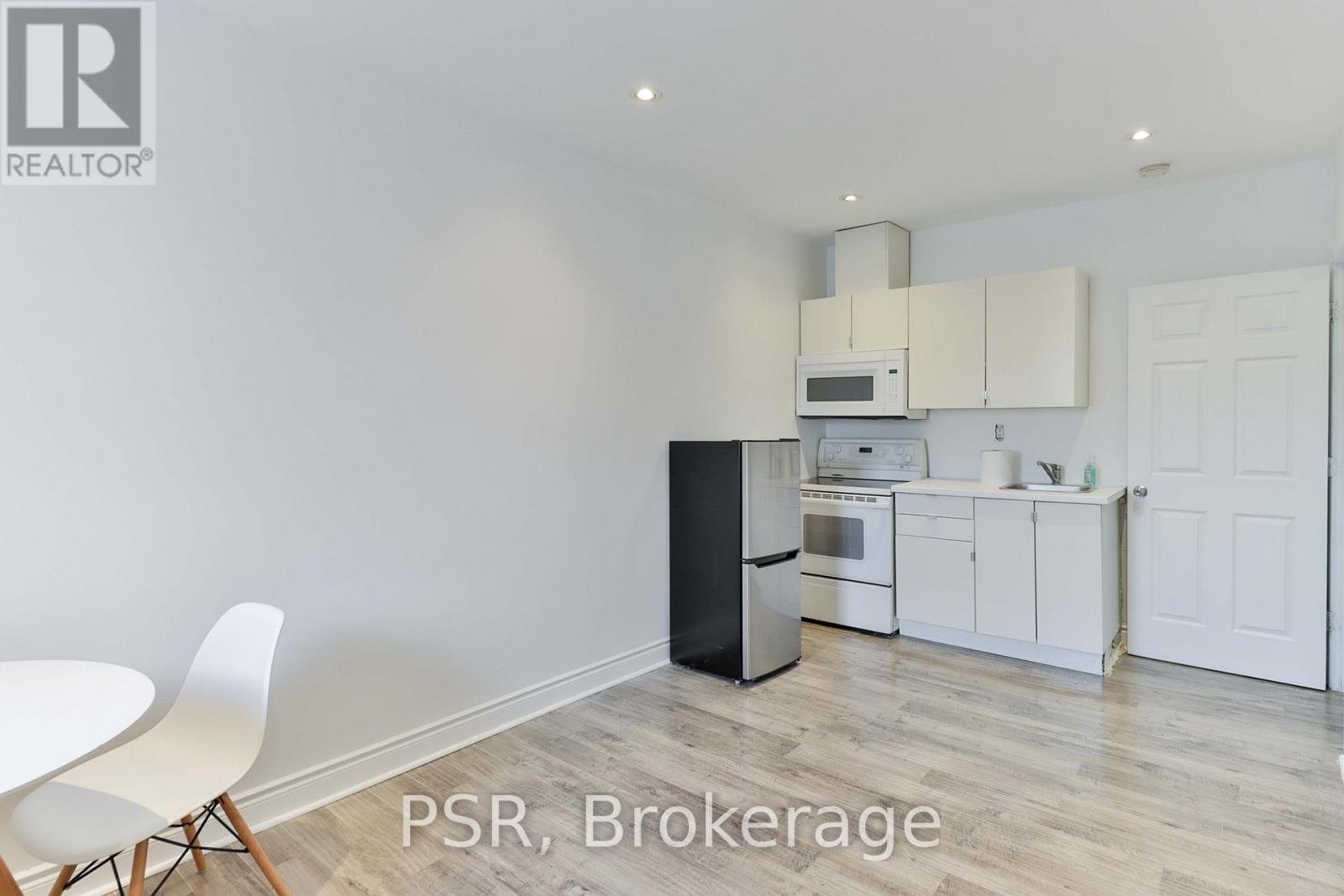 A kitchen with a black fridge, white cabinets, and a white table.
