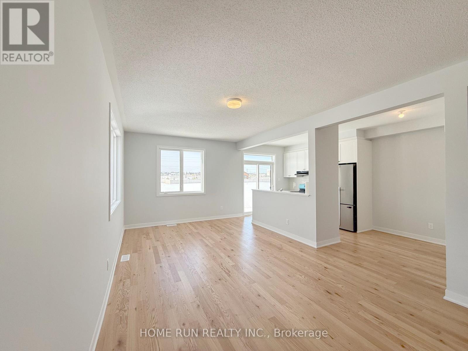 A spacious room with wooden flooring and white walls, with a refrigerator visible in the corner.