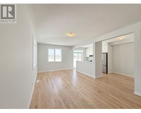 A spacious room with wooden flooring and white walls, with a refrigerator visible in the corner.