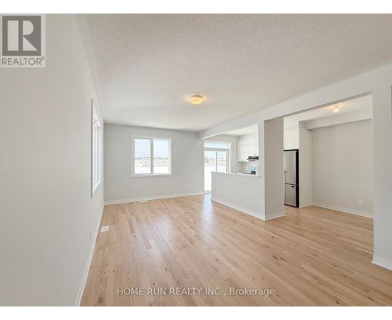 A spacious room with wooden flooring and white walls, with a refrigerator visible in the corner.
