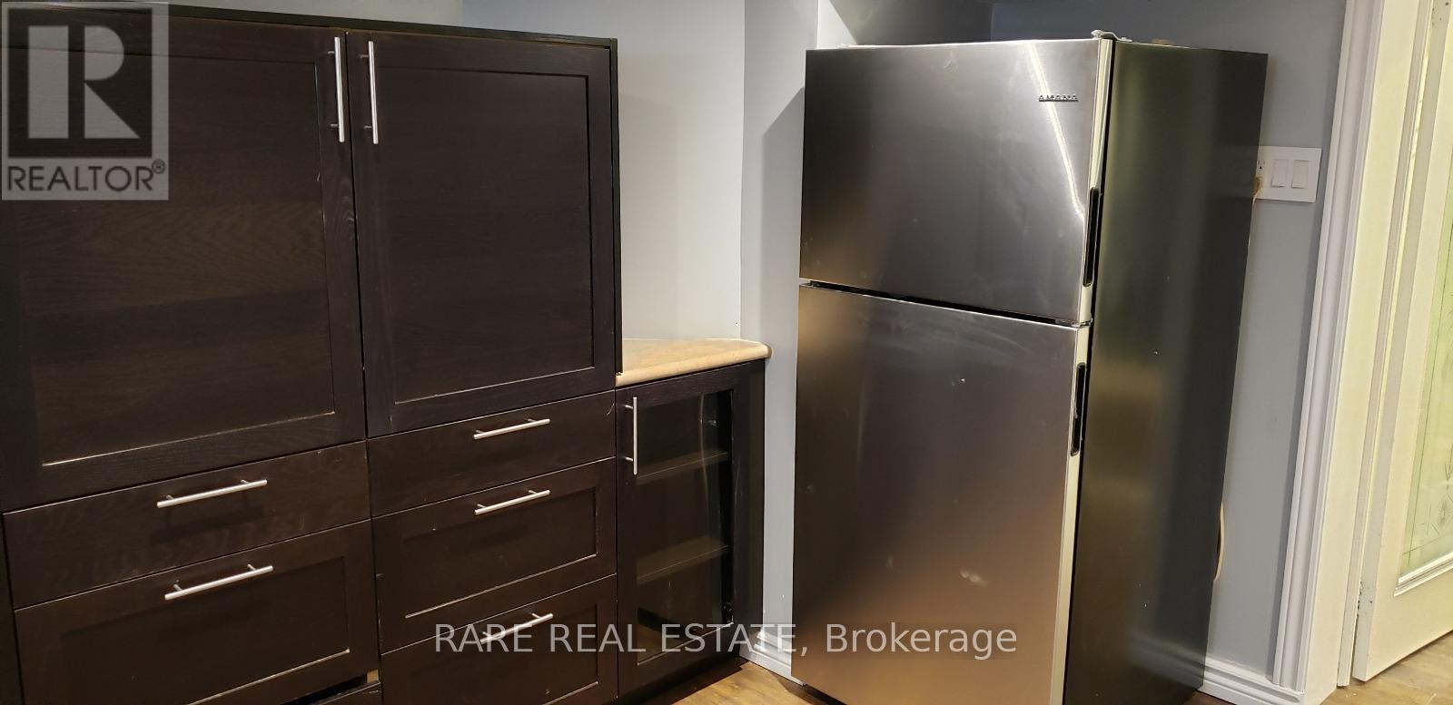 A stainless steel refrigerator stands next to a wooden cabinet.