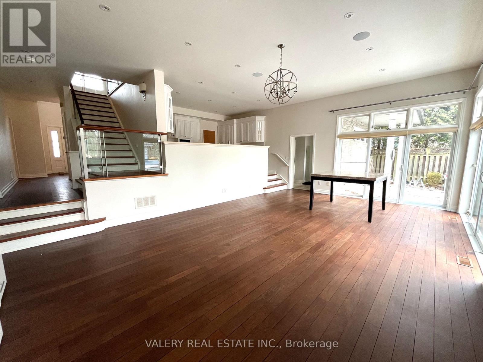 A spacious room with wooden flooring and a staircase in the background.