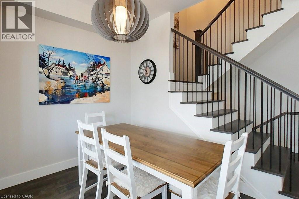 A dining room with a wooden table and chairs, a staircase, and a painting on the wall.