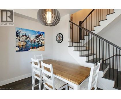 A dining room with a wooden table and chairs, a staircase, and a painting on the wall.