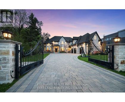 A gated entrance to a large, luxurious house with a stone pathway leading to the gates.