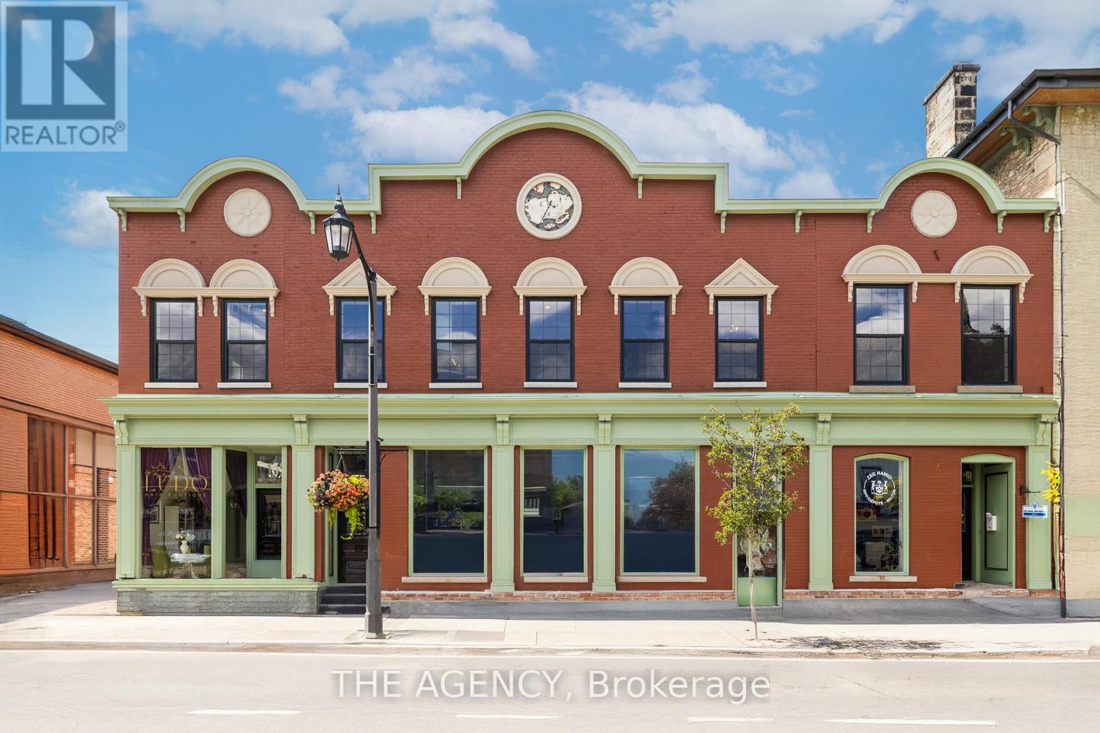 A red brick building with green trim and a sign that says "The Agency Brokerage".