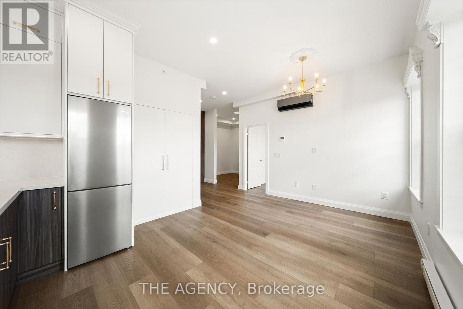 A spacious room with wooden flooring and a stainless steel refrigerator.