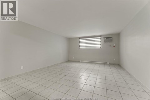 A spacious empty room with tiled flooring and white walls.
