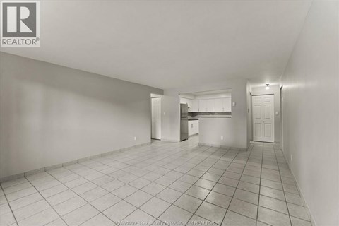 A spacious empty room with tiled flooring and white walls.