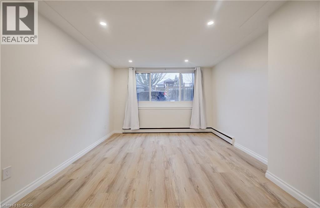 A spacious room with wooden flooring and a window with white curtains.
