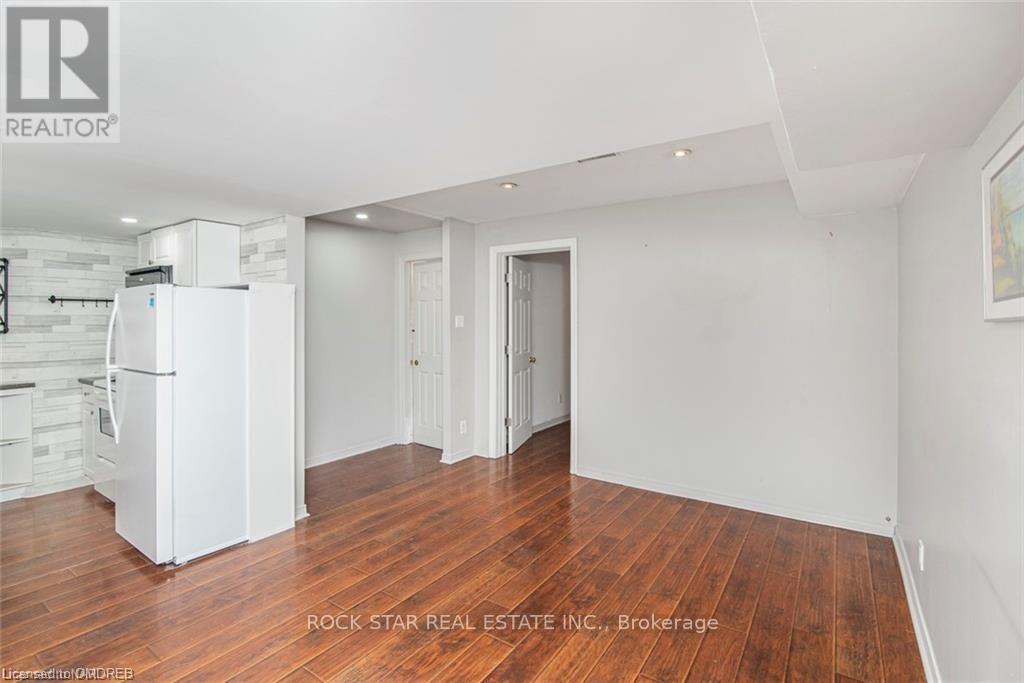 A spacious room with wooden flooring and white walls, featuring a refrigerator and a cabinet.