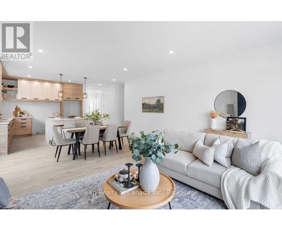 A modern living room with a white sofa, a wooden coffee table, and a dining area in the background.