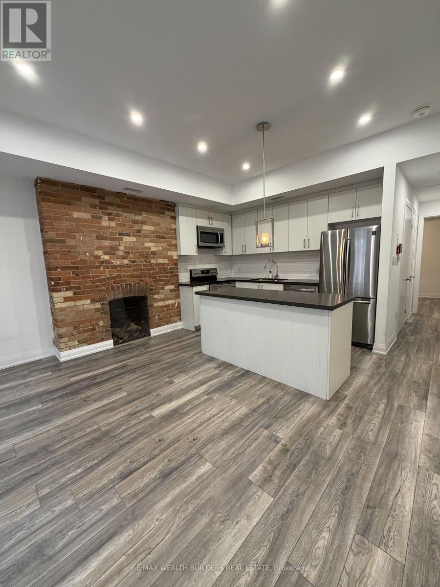 A modern kitchen with a brick accent wall and wood flooring.