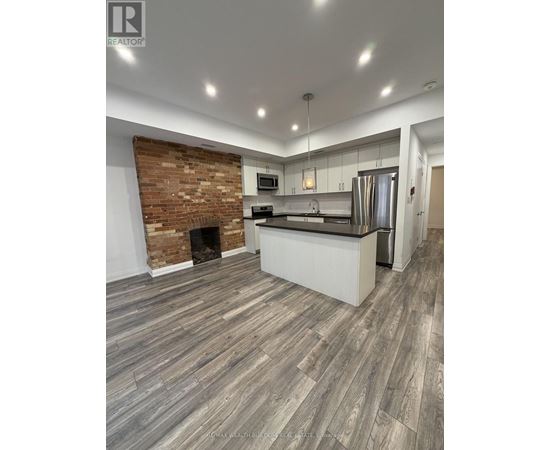 A modern kitchen with a brick accent wall and wood flooring.