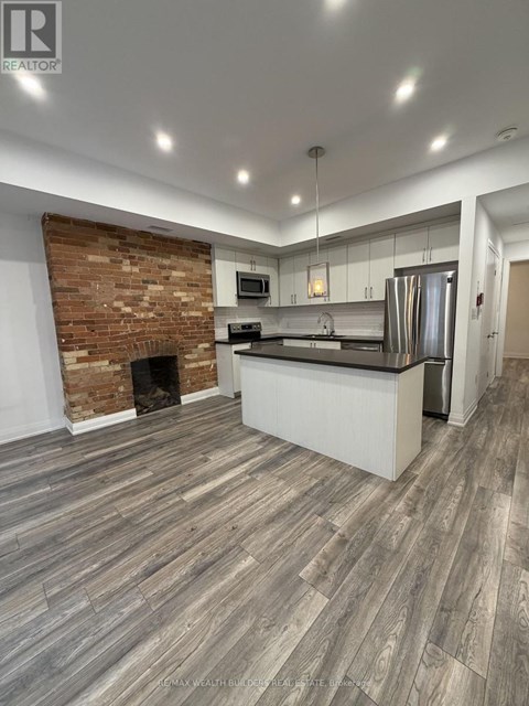 A modern kitchen with a brick accent wall and wood flooring.