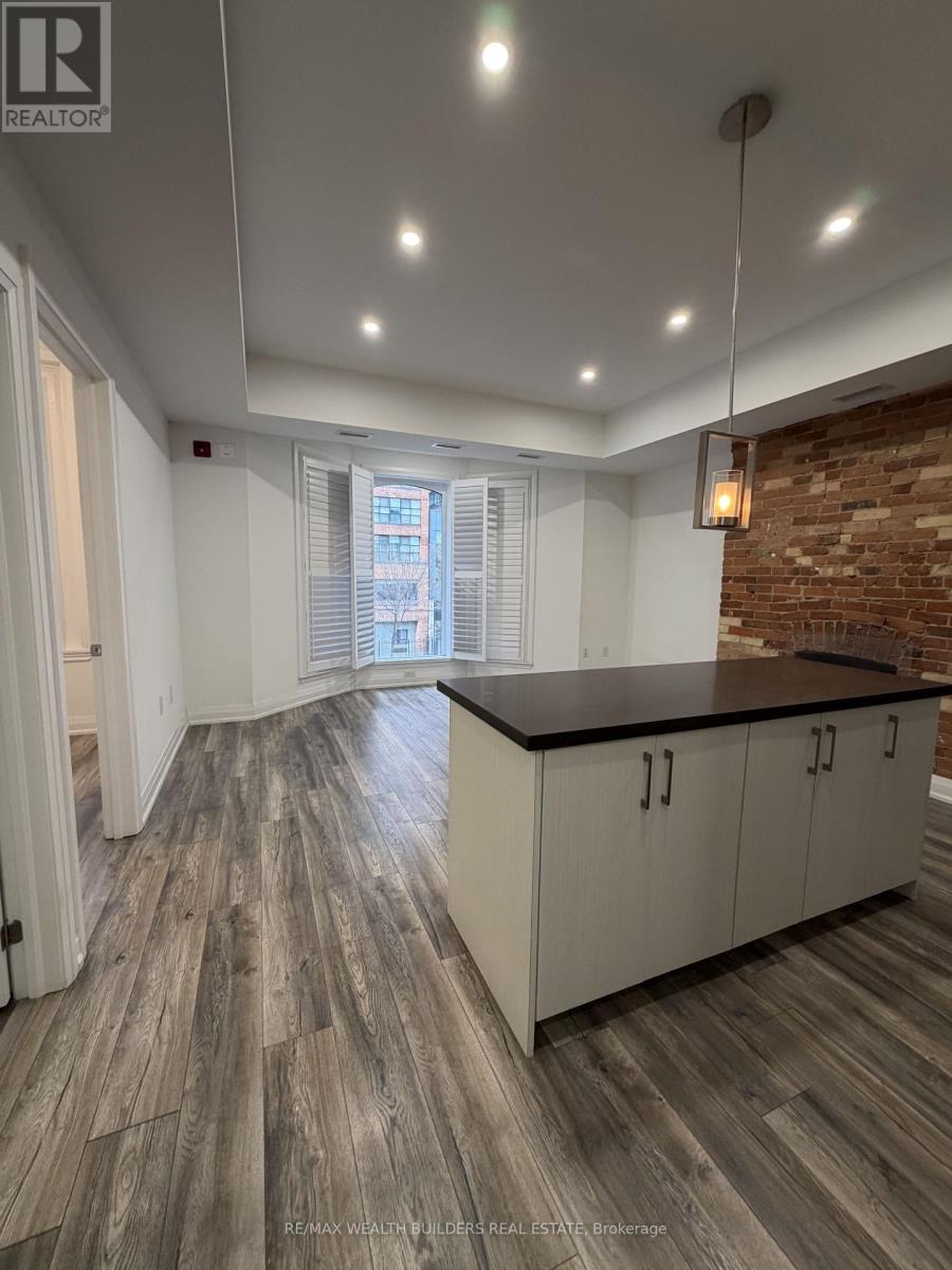 A spacious kitchen with wooden flooring and a brick accent wall.
