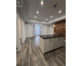A spacious kitchen with wooden flooring and a brick accent wall.