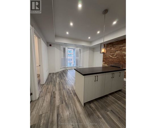 A spacious kitchen with wooden flooring and a brick accent wall.