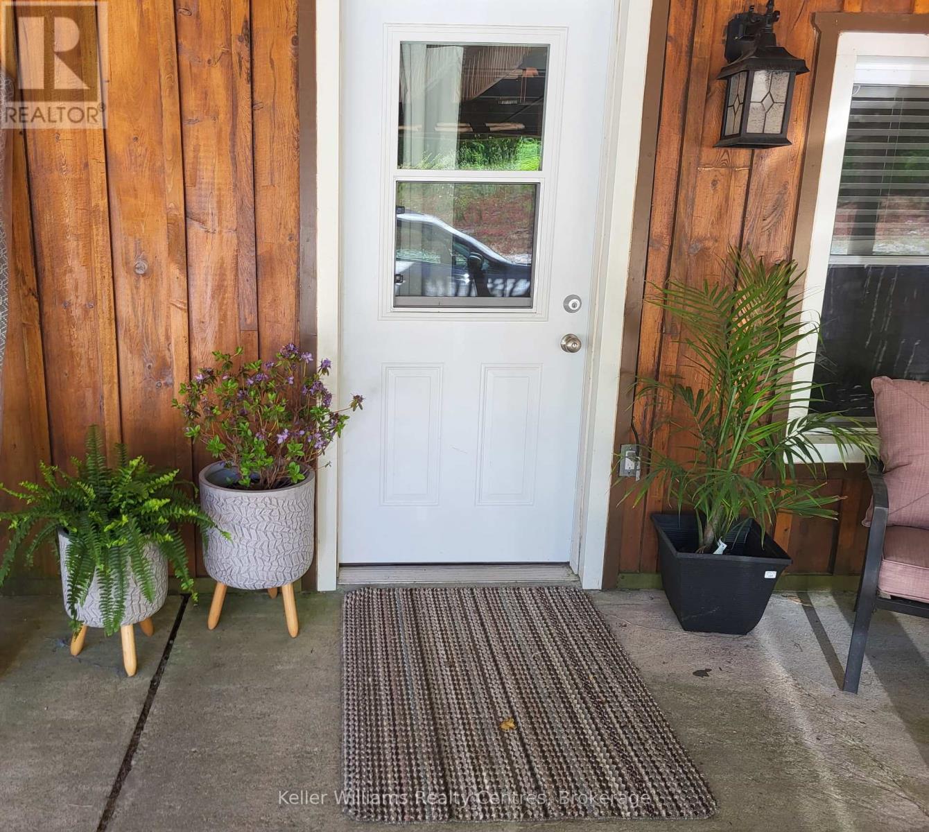 A white door is flanked by two potted plants and a rug.