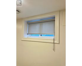A window with white blinds and a curtain is in a white room.