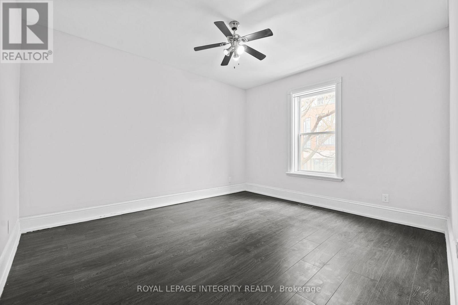 A room with a ceiling fan and a window showing a building outside.