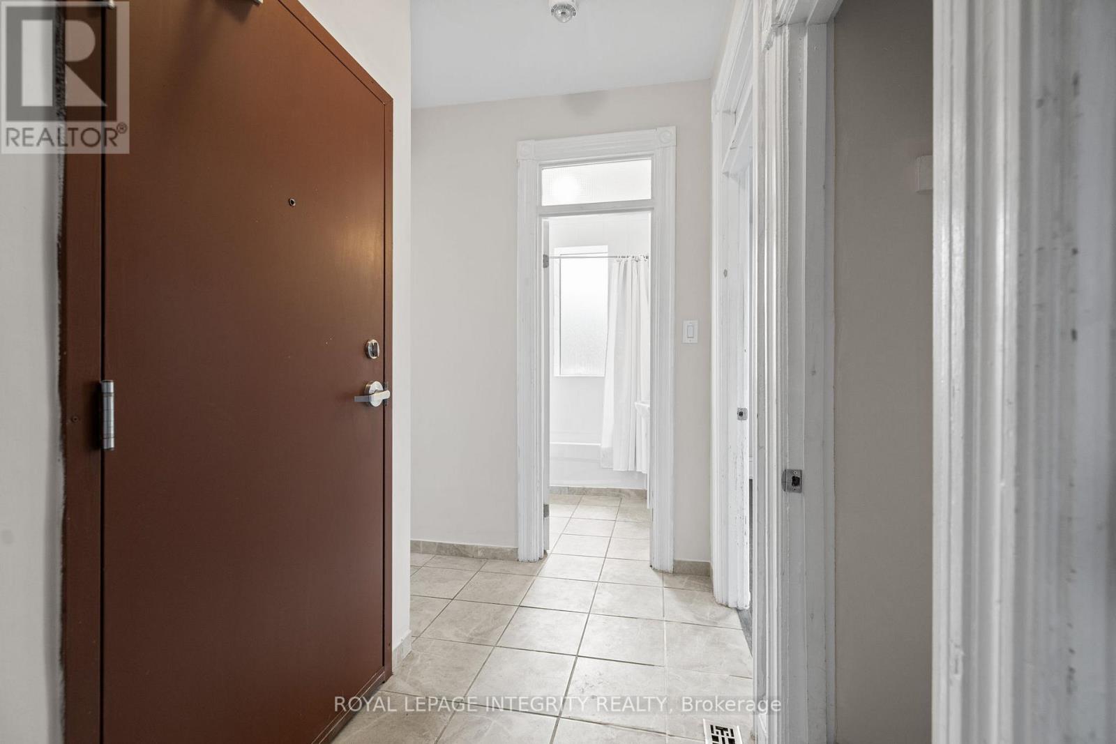 A brown door is on the left of a white hallway.
