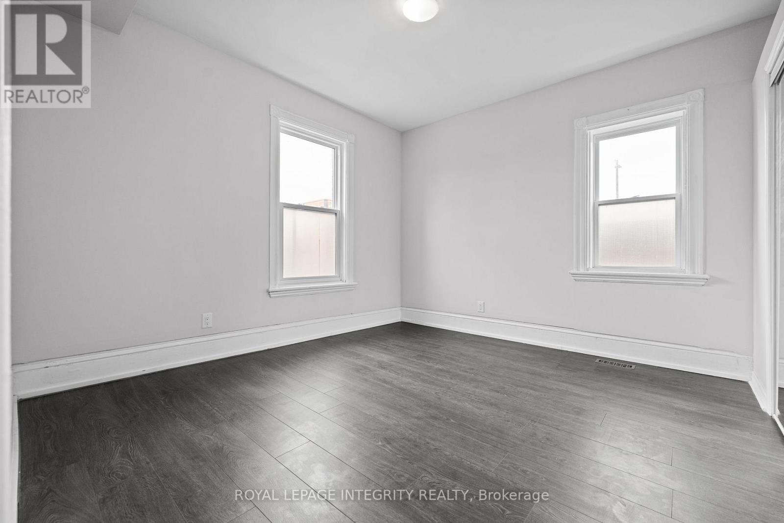 A spacious room with wooden flooring and two windows.