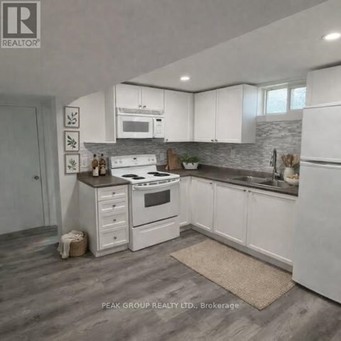 A kitchen with white cabinets and appliances, a stone backsplash, and a rug on the floor.