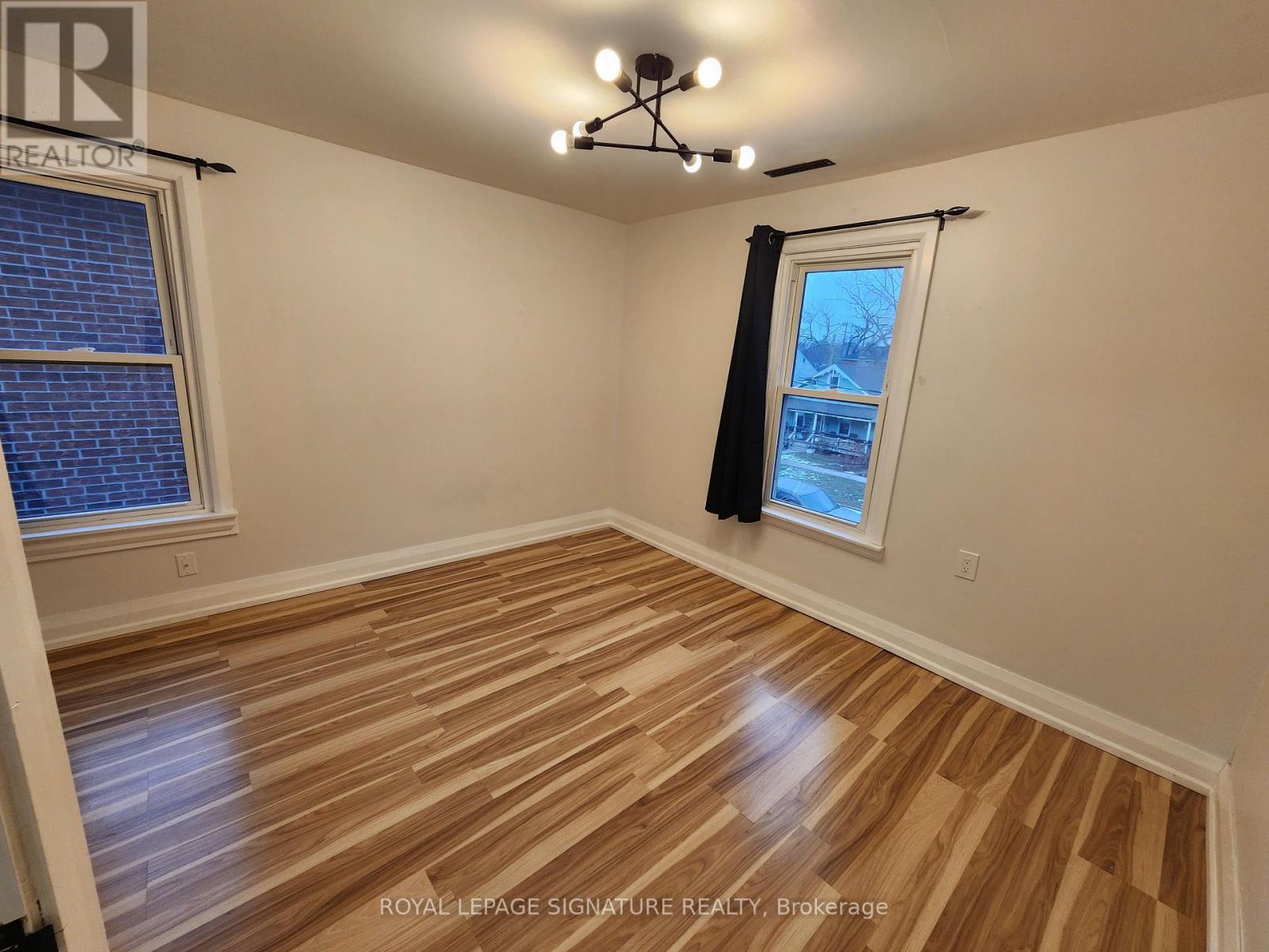 A room with wooden flooring and a window with a view of a house.