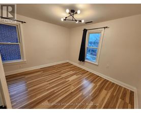 A room with wooden flooring and a window with a view of a house.