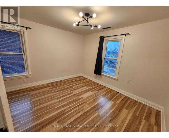 A room with wooden flooring and a window with a view of a house.
