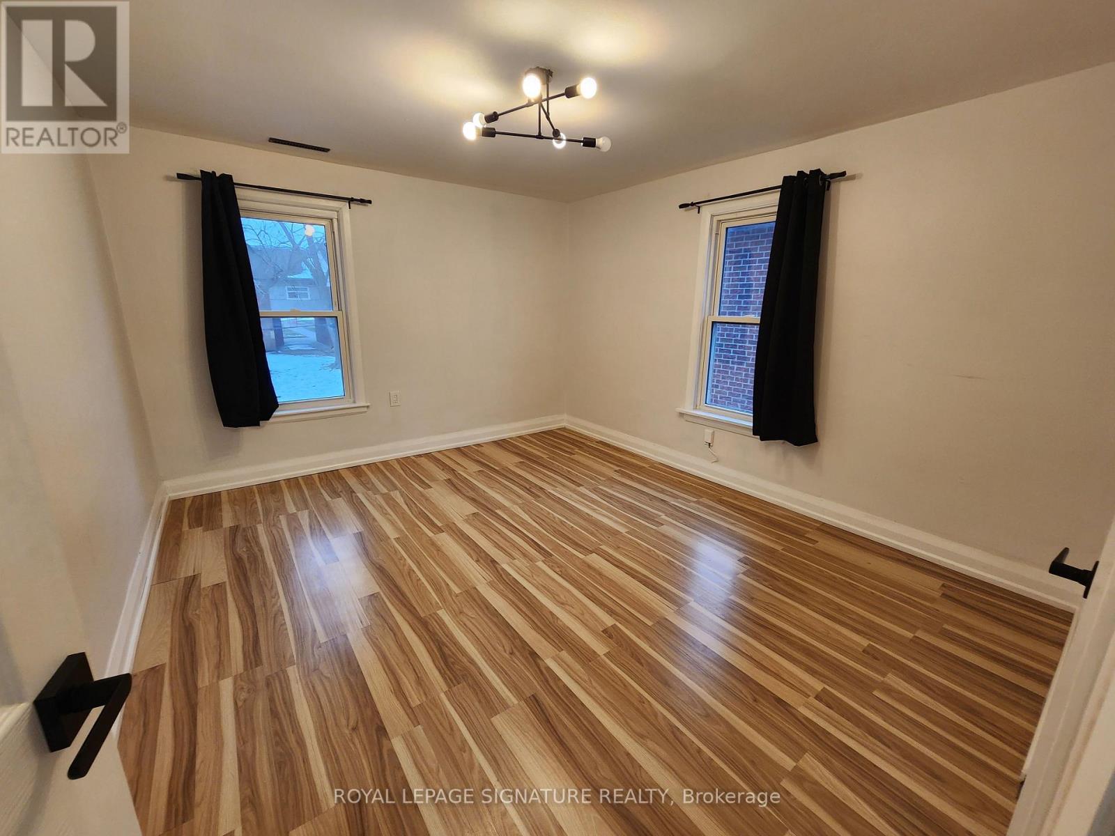 A room with wooden flooring and two windows with black curtains.