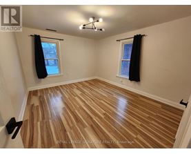 A room with wooden flooring and two windows with black curtains.