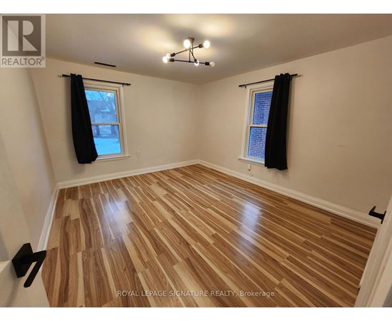 A room with wooden flooring and two windows with black curtains.