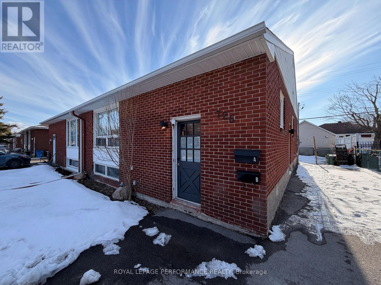 A red brick building with a black door and windows, surrounded by snow.